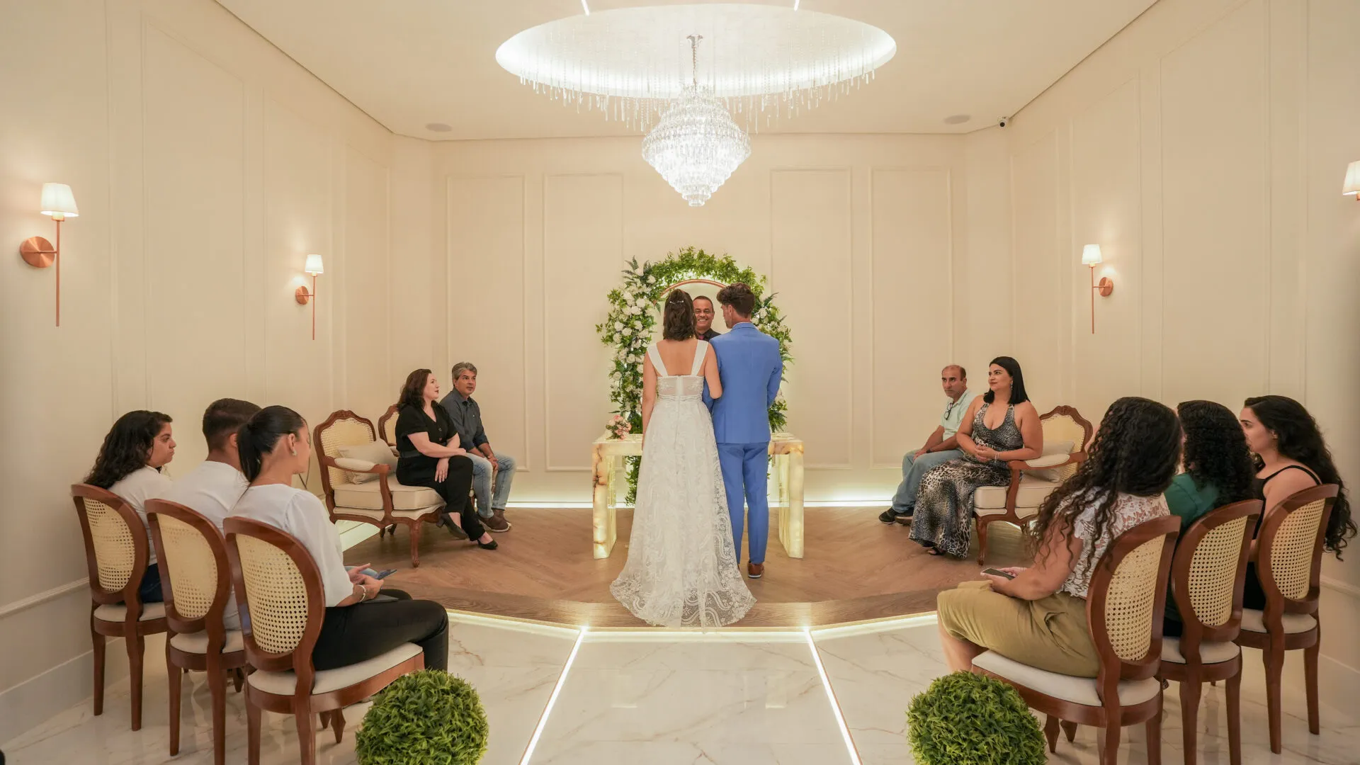 Cerimônia de casamento civil na sala de celebrações do 1º Cartório, com os noivos diante do arco floral e convidados sentados